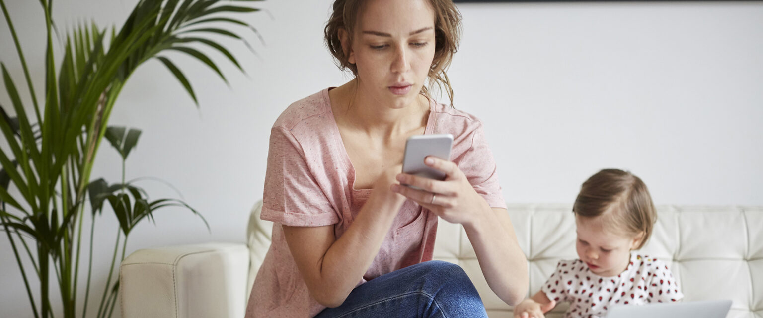 Eine junge Frau sitzt auf einem weißen Sofa an ihrem Handy